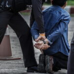 A man experiencing false arrest kneeling on the ground and being handcuffed