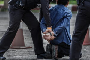 A man experiencing false arrest kneeling on the ground and being handcuffed
